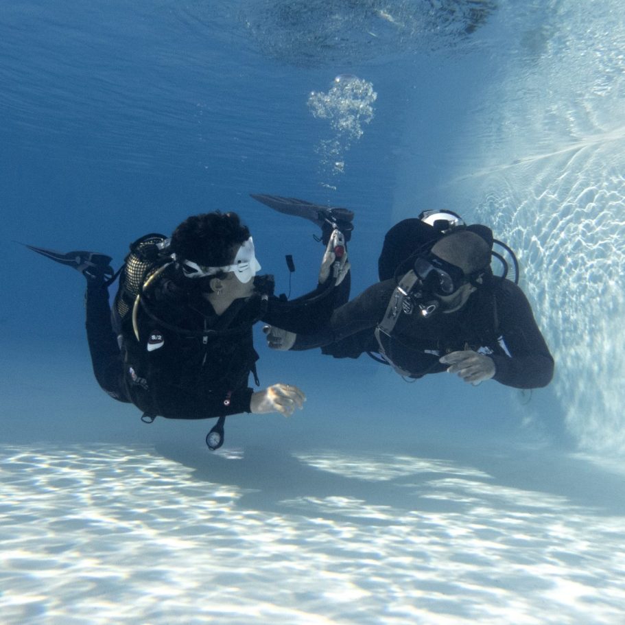 Dos buzos se sumergen en una piscina, sosteniendo equipos de buceo y aprendiendo