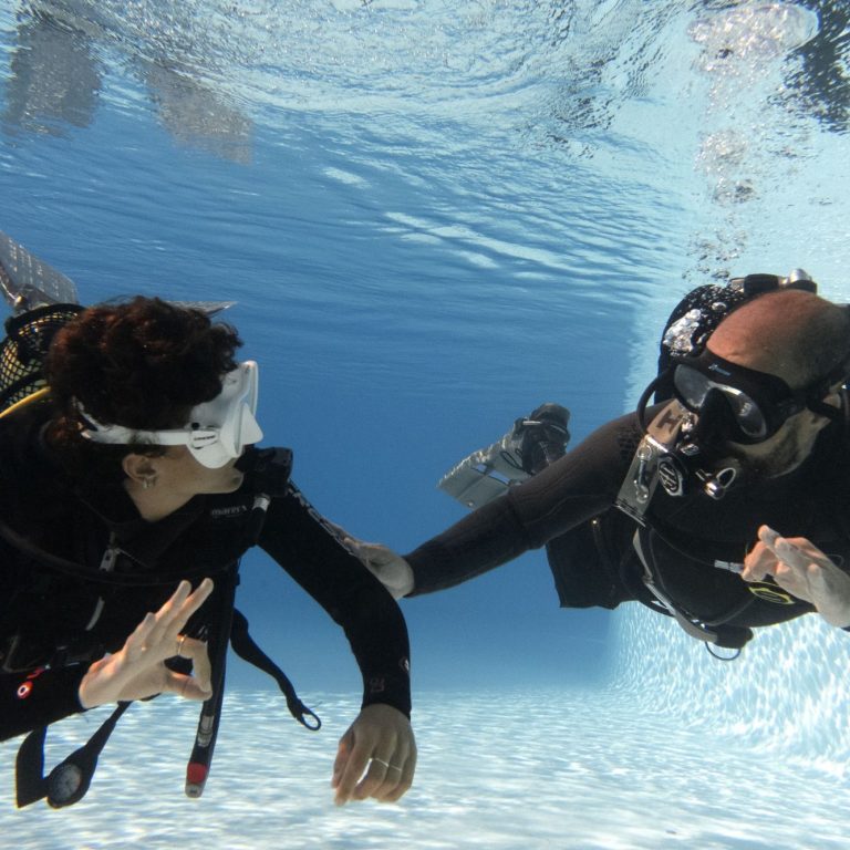 prácticas en piscina un instructor de buceo ayuda a otro a estar relajado en la piscina.