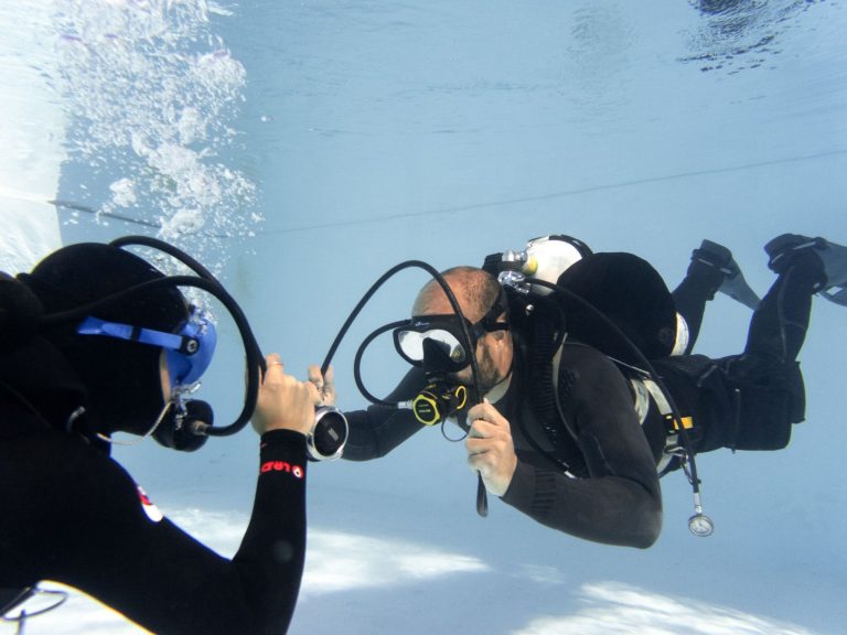 Dos buceadores en el agua, usando equipo de buceo con configuración hogarthiana, practicando ejercicios.
